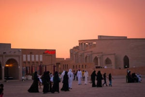 There are people walking around the village with one restaurant and the amphitheatre in the background.