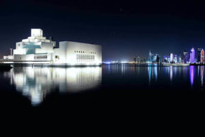 The museum building and Qatar skyline in the evening light, with building reflected in the body of water.