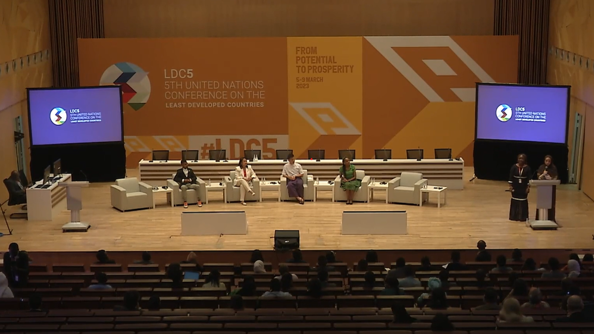 Stage of Youth Forum at the Fifth UN Conference on the Least Developed Countries showing a panel of speakers in front of a conference backdrop, with Moza AlHajri and her co-moderator standing at a podium to the right of the stage.